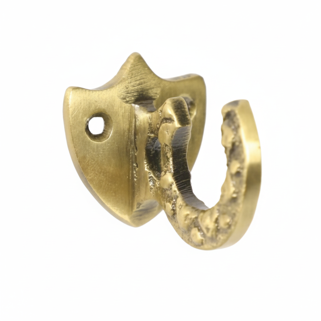 A decorative wall hook featuring a shield-shaped backplate and a textured curved hook in a brushed antique brass finish. The design includes two pre-drilled mounting holes for secure installation on walls, cabinets, or wardrobes.