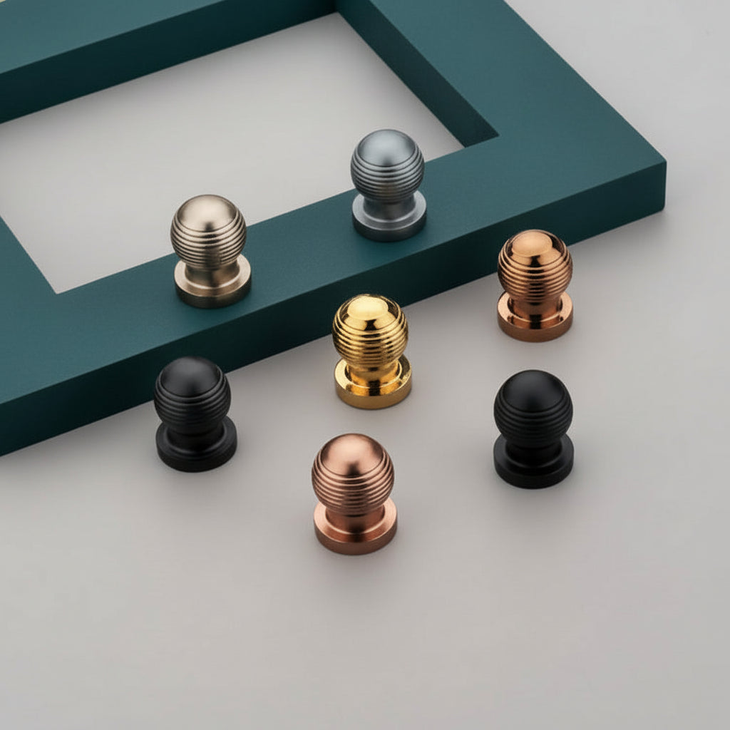 A collection of Creatick KB-01 modern ribbed cabinet knobs displayed in various finishes including matte black, satin gold, rose gold, and silver. These round, textured furniture knobs are arranged on a minimalist grey surface with a decorative teal frame, showcasing luxury hardware options for drawers, cupboards, and kitchen cabinets.