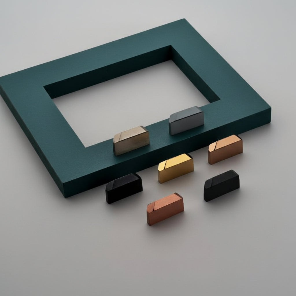 A variety of Creatick KB-67 minimalist geometric cabinet knobs featuring a unique slanted-top design. The collection is shown in elegant finishes including matte black, gold, rose gold, and gunmetal grey, displayed on a professional display surface for luxury furniture and contemporary kitchen hardware inspiration.