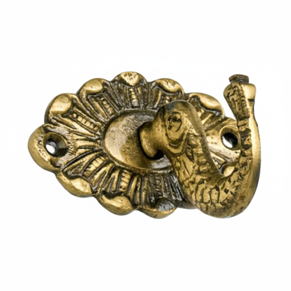 An ornate decorative wall hook featuring a detailed elephant head with an upturned trunk serving as the hook, mounted on a scalloped oval backplate with radial engravings and an antique brass finish. The piece includes two pre-drilled holes for secure wall mounting.