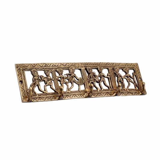 An antique brass wall hook rack featuring traditional Dhokra tribal art with handcrafted metal figures of musicians and dancers within a rectangular frame, equipped with five hooks for keys or lightweight accessories.