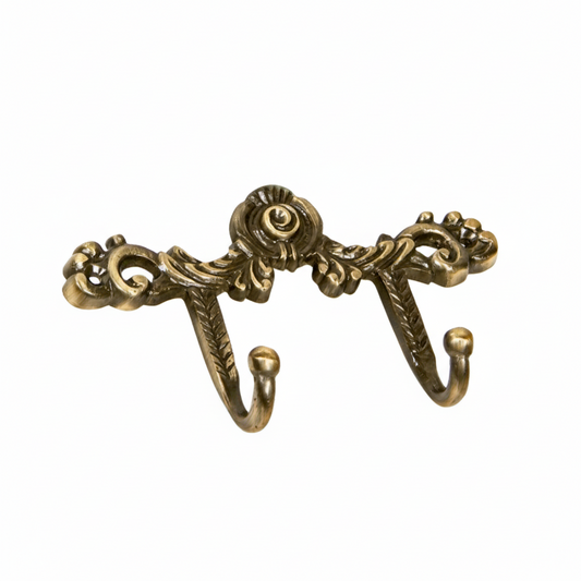 An ornate Victorian-style double wall hook featuring intricate scrollwork, a central rose motif, and acanthus leaf details in an antique brass finish. The decorative metal hardware includes two curved hooks with ball tips, perfect for hanging coats or accessories in a luxury interior.