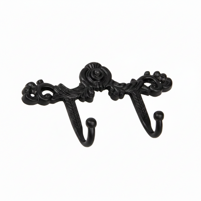 An ornate Victorian-style double wall hook featuring intricate scrollwork, a central floral rose motif, and acanthus leaf details in a sleek black finish. The decorative metal hardware includes two curved hooks with smooth ball tips, designed for hanging coats or accessories in a modern or classic interior.