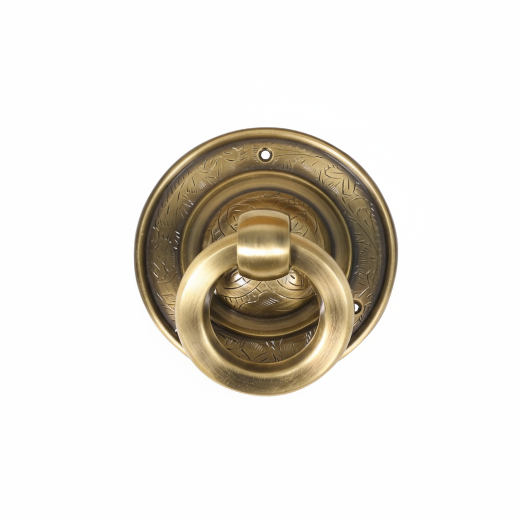 A traditional round ring pull handle made of antique brass, featuring a thick circular ring attached to a decorative backplate with intricate etched floral patterns and pre-drilled mounting holes for furniture and cabinet installation.