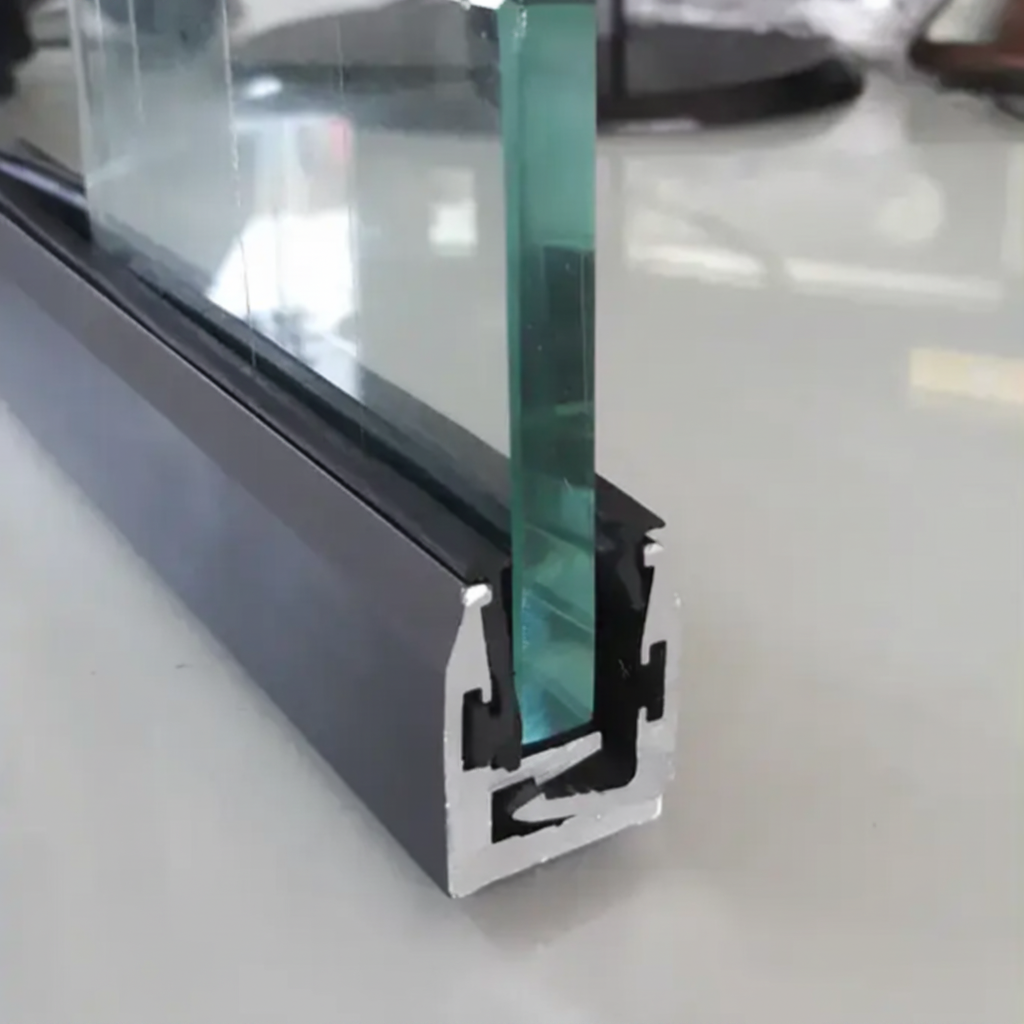 A close-up of a black anodized aluminum interlocking glazing profile holding a thick tempered glass panel. The image demonstrates the secure U-channel mounting system with internal rubber gaskets and interlocking clips, ideal for frameless glass office partitions, shower enclosures, and modern architectural glass railing installations.