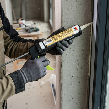 A construction professional using an Eternity heavy-duty caulking gun to apply a precise bead of silicone sealant between a concrete wall and a black window frame. The image demonstrates the tool's ergonomic grip and smooth dispensing action in a real-world building environment, highlighting its effectiveness for waterproof sealing and architectural glazing tasks.