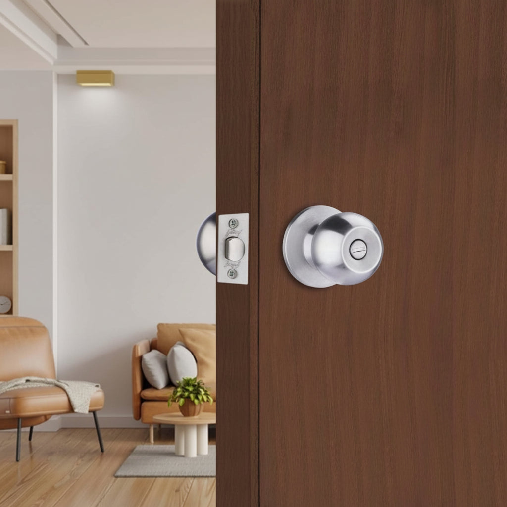 Godrej cylindrical privacy door lock with a brushed satin finish and emergency release slot, installed on a rich mahogany-finished wood door within a contemporary, sunlit residential living area.