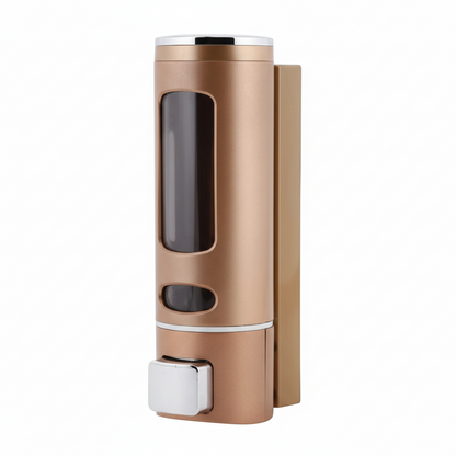 Grafiqe wall-mounted cylindrical liquid dispenser in a matte champagne rose  gold finish, featuring a large transparent viewing window for level monitoring and a chrome manual push-button pump for shower or vanity organization.