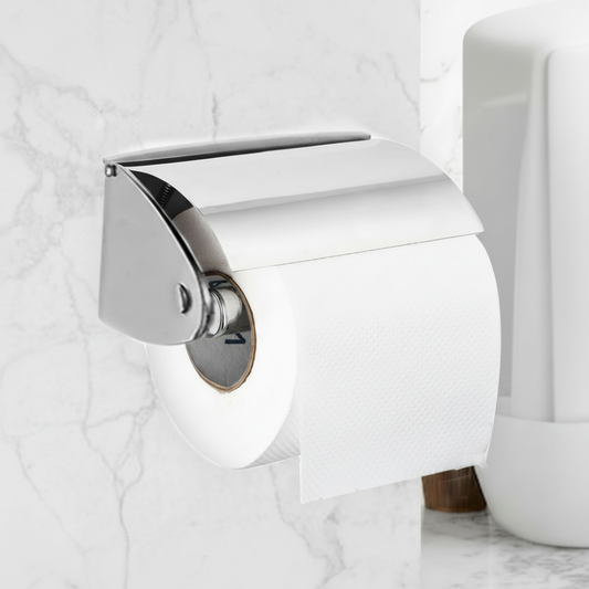 Close-up lifestyle view of a Grafiqe wall-mounted toilet roll holder in a polished chrome finish with a protective flap cover, installed on a white marble wall in a modern luxury bathroom.