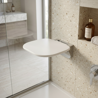 Lifestyle view of a Grafiqe curved white wall-mounted shower seat with a polished chrome bracket, installed on a beige terrazzo tile wall next to a built-in shower niche and glass partition in a luxury bathroom.