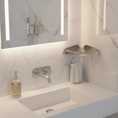 Lifestyle view of a Grafiqe perforated stainless steel corner shelf installed on a white marble-tiled wall, positioned next to a backlit bathroom mirror and modern brushed metal faucet for high-end vanity organization.