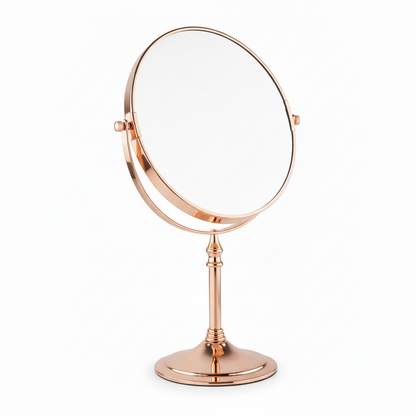 Grafiqe circular pedestal tabletop mirror in a premium rose gold finish, featuring a 360-degree double-sided swivel head for standard and magnifying views on an elegant stem and a stable weighted base.