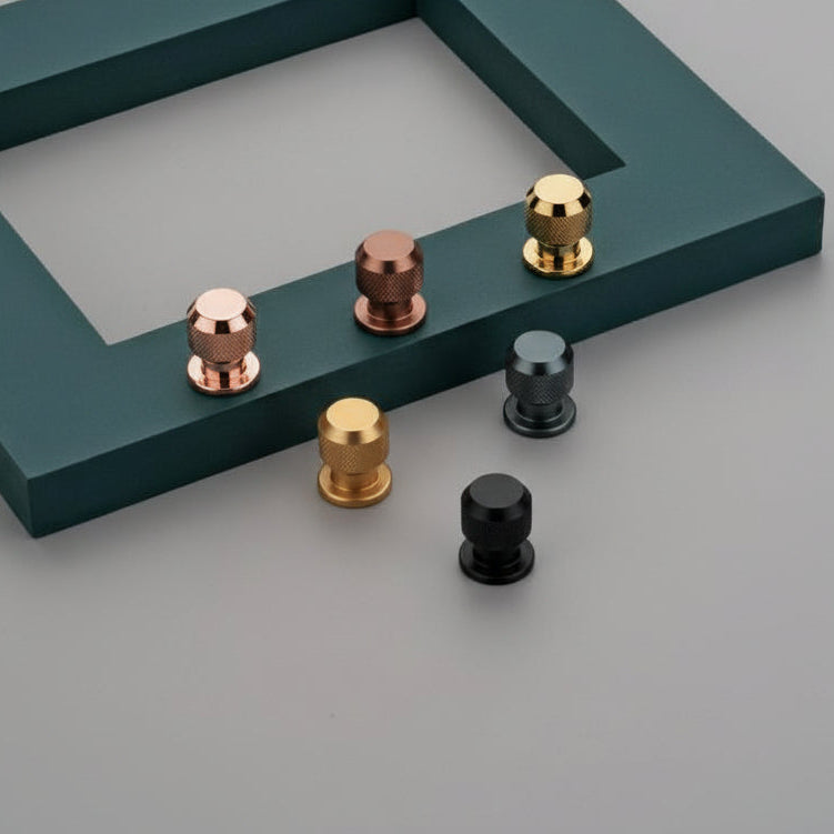 A group of Creatick KB-06 modern knurled pedestal knobs with a textured diamond grip. These round industrial-style furniture knobs are shown in various finishes, including matte black, polished gold, rose gold, and gunmetal gray, displayed against a minimalist gray and teal background for high-end cabinet and drawer hardware inspiration.