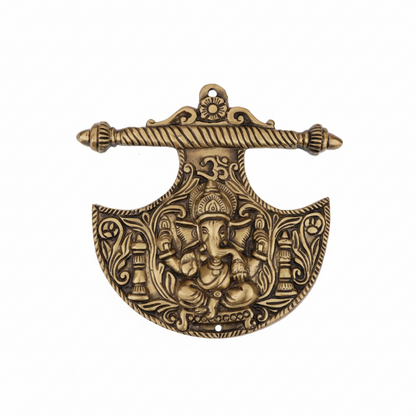 An antique brass wall-hanging accent in the shape of a Parashu (axe) featuring a central Lord Ganesha icon, a sacred Om symbol, and intricate floral carvings, designed for home temple decoration or Vastu protection at the main entrance.