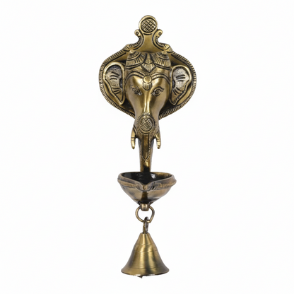 An antique brass wall-mounted hanging oil lamp (diya) featuring a Lord Ganesha head backplate with a single oil wick bowl and a hanging puja bell, designed for home temple or pooja room decoration.